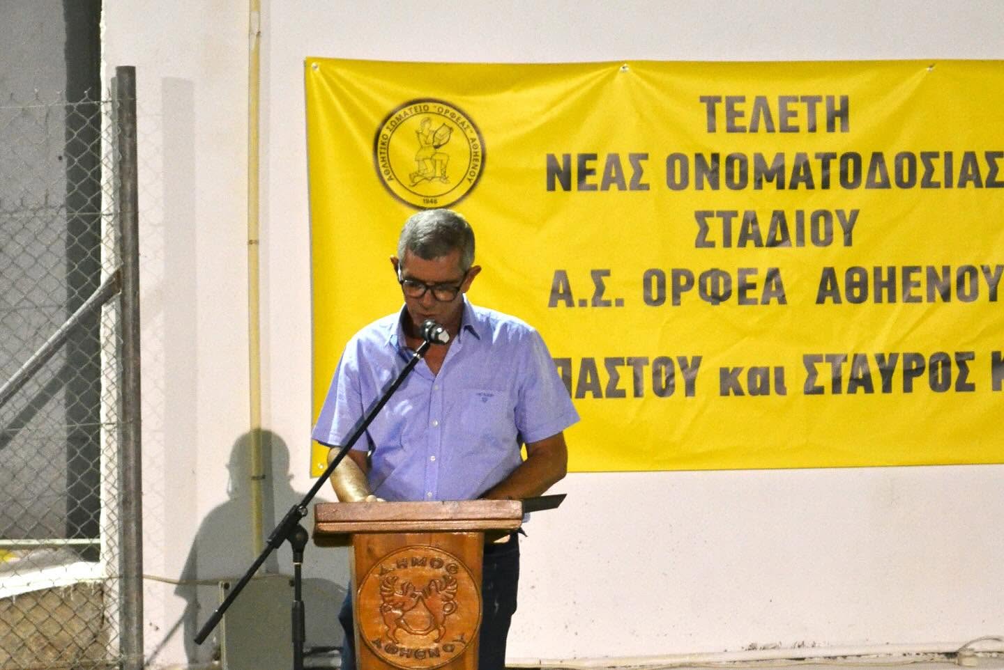 A man speaking at a wooden lectern in front of a yellow banner of the association