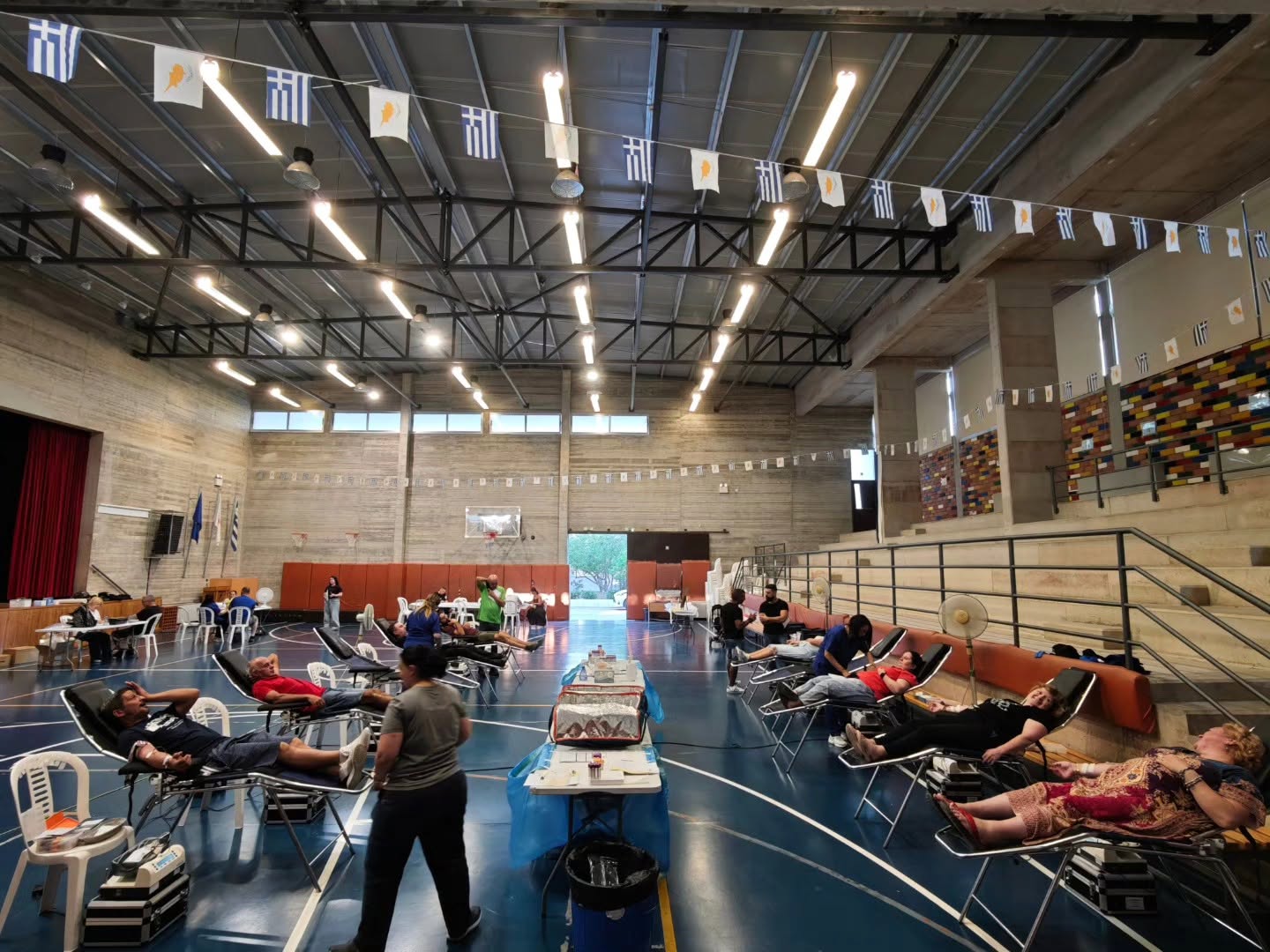 A blood donation session taking place inside an indoor sports hall decorated with flags